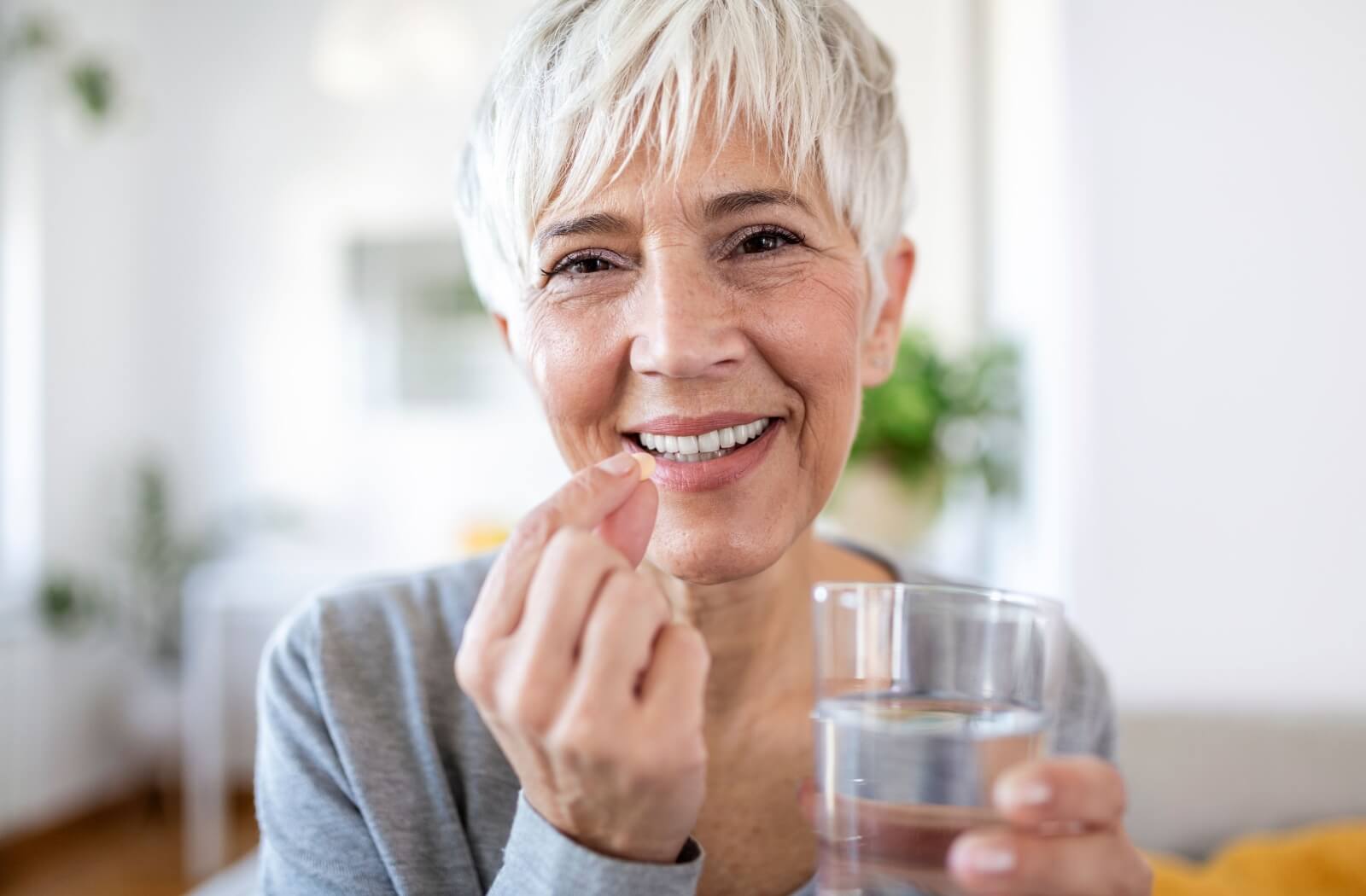 Smiling older adult taking vitamins with a glass of water.
