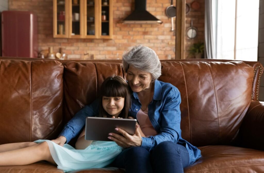 An older adult and their grandchild cuddle on the couch while using a tablet to play an online mind game.
