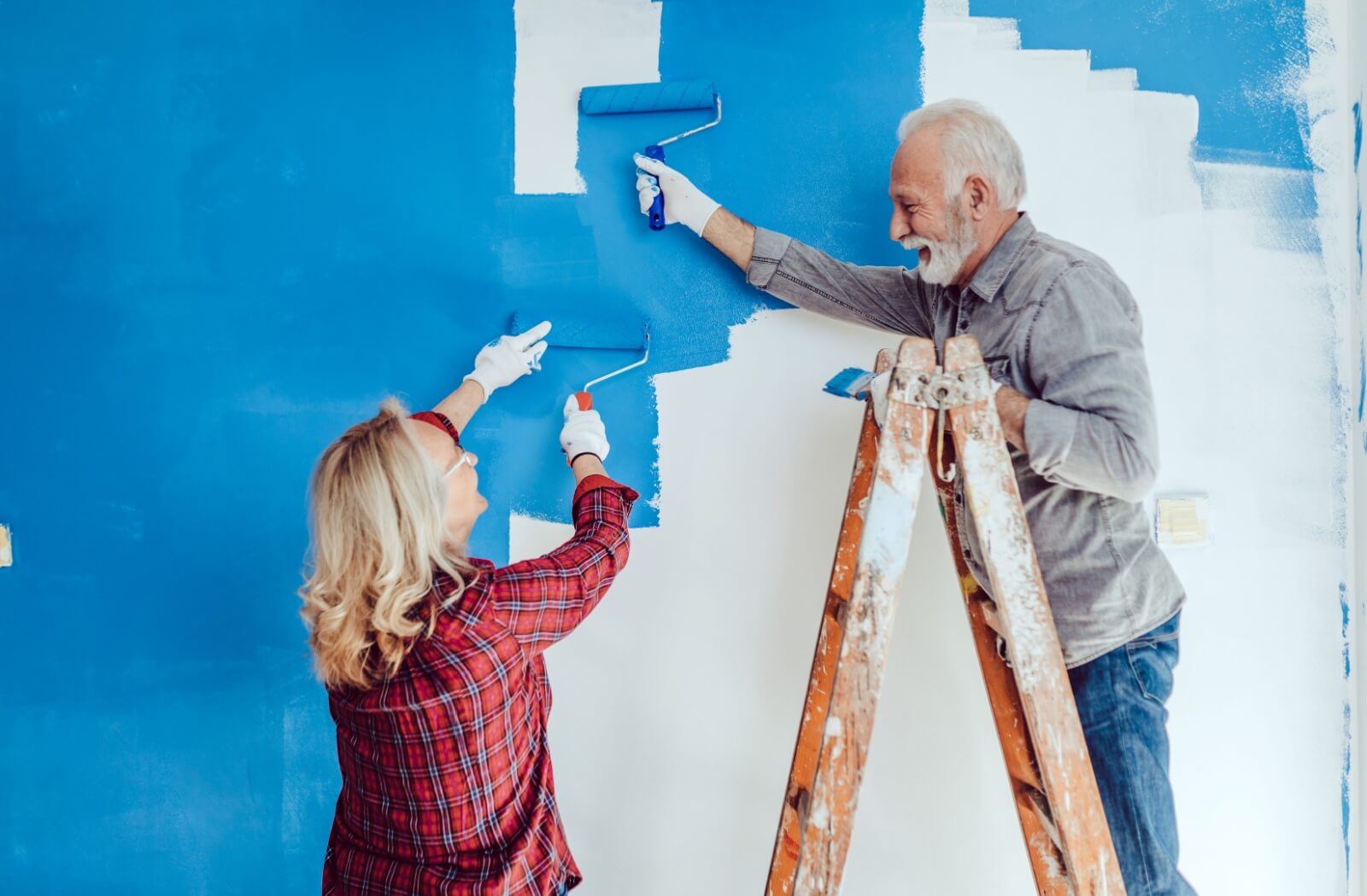 Two older adults paint the walls of their apartment blue.