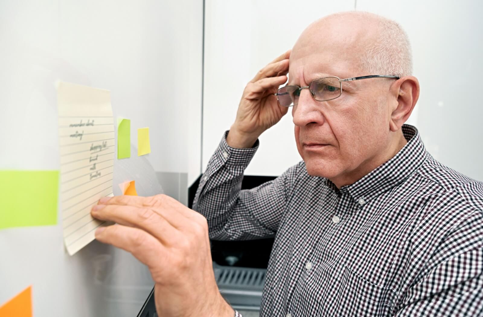 A confused older adult looks at a note they wrote for themself.