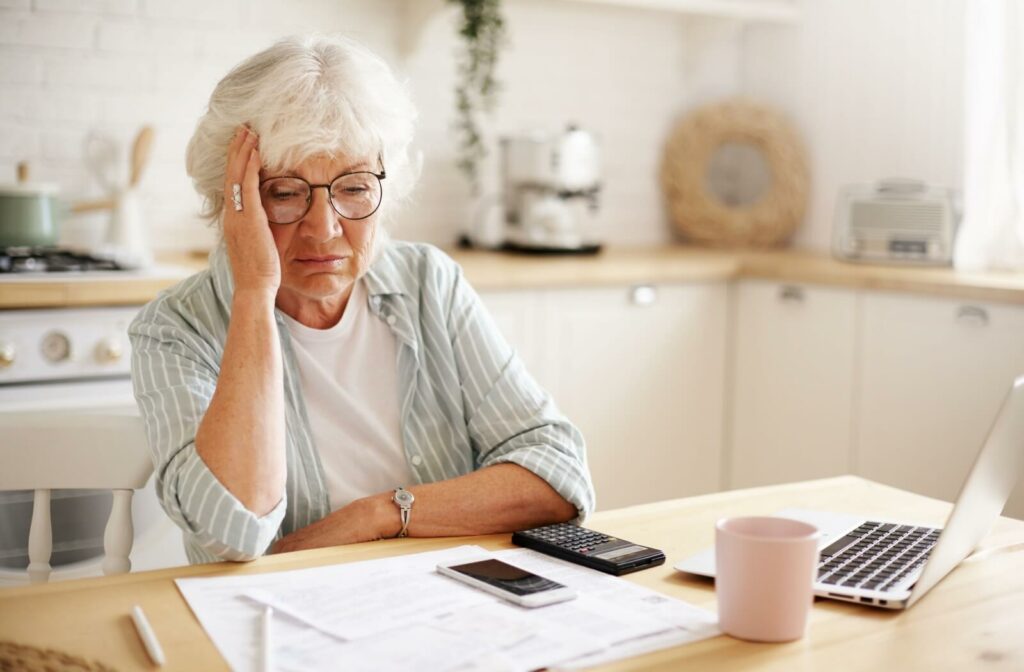 A frustrated older adult tries to pay bills online but takes a break, resting their head in their hand.