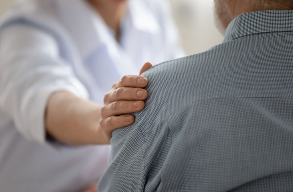 A concerned caregiver places their hand on an older adult's shoulder.