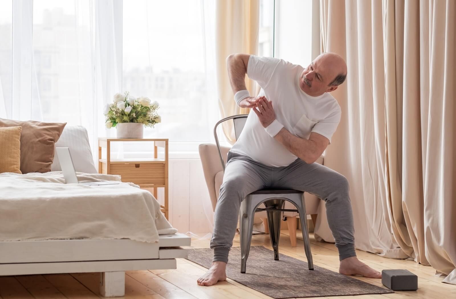 An older adult performs chair yoga guided by an online video in their assisted living apartment.