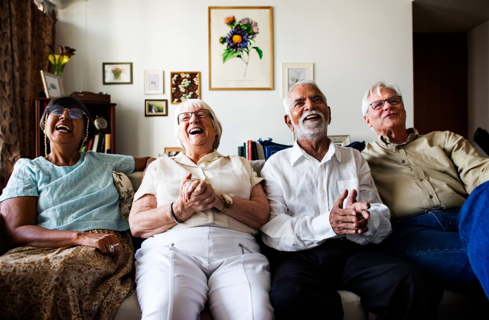 A cheerful group of older adults laughing together on a cozy couch in an assisted living community.