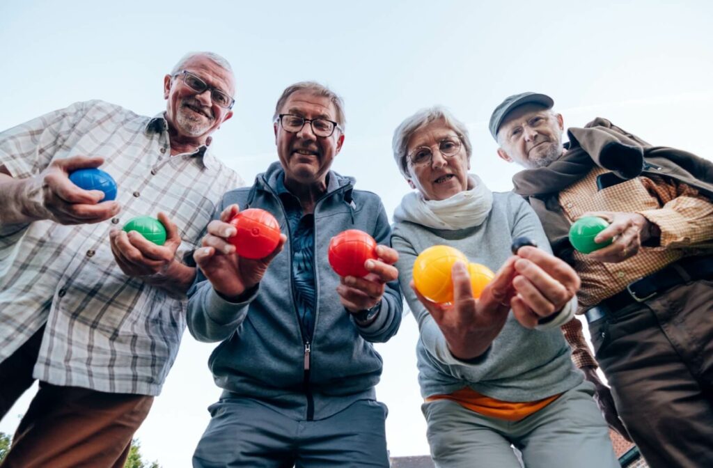 A lively group of older adults smiling for the camera with their lawn bowling balls.