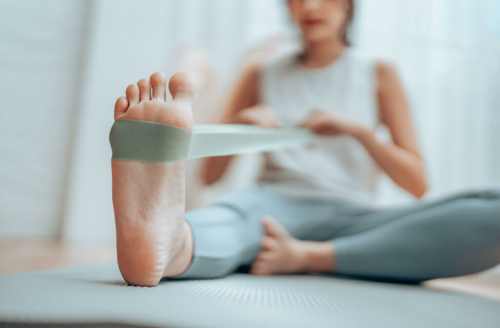 An older adult stretches their leg by looping a resistance band around their foot, pulling the band back with both arms.