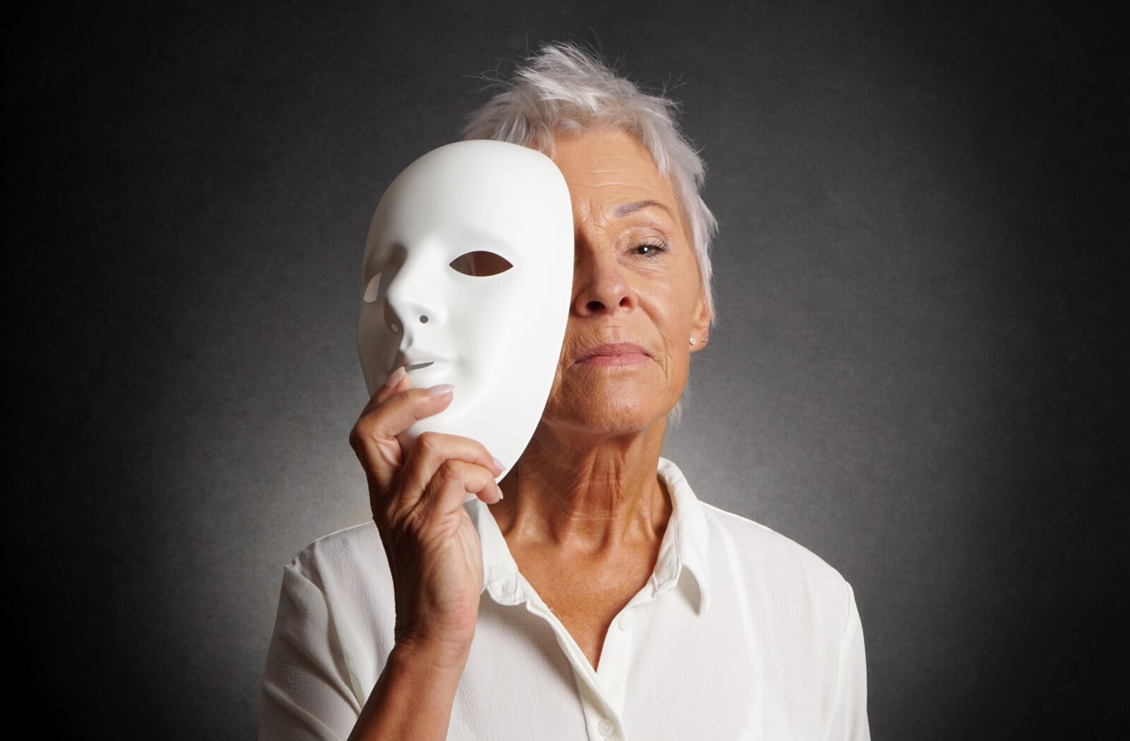 A serious-looking person holds a theatre mask over one half of their face.