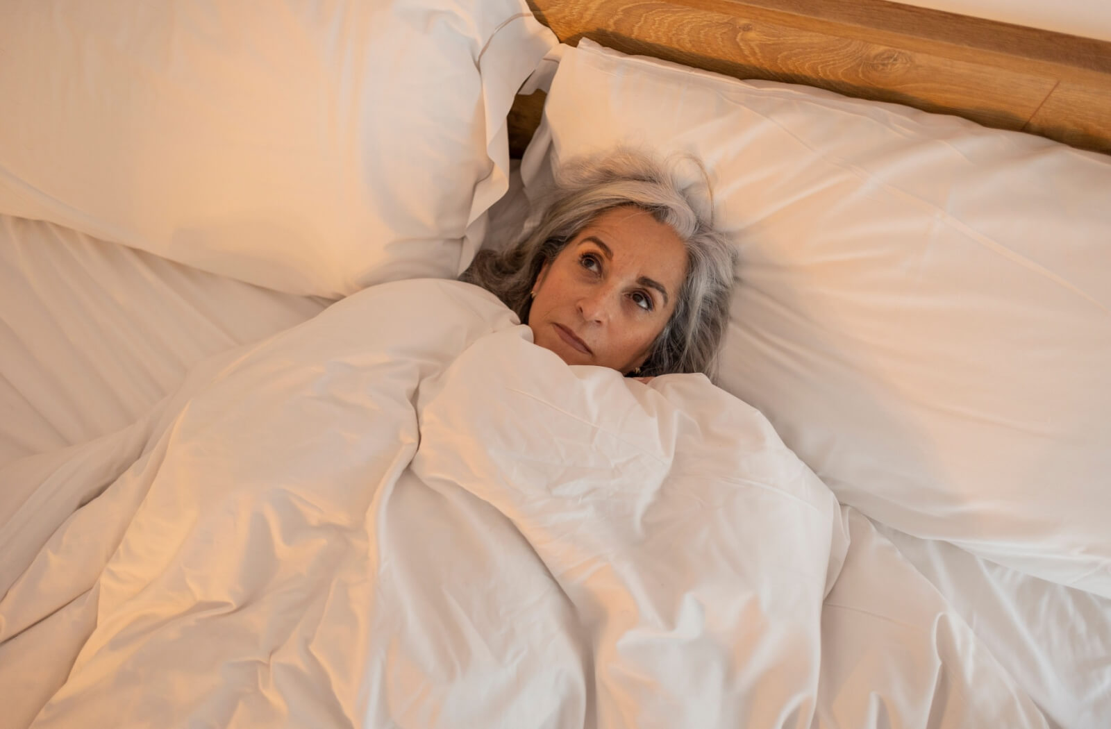 An older adult lies in bed, struggling to sleep.