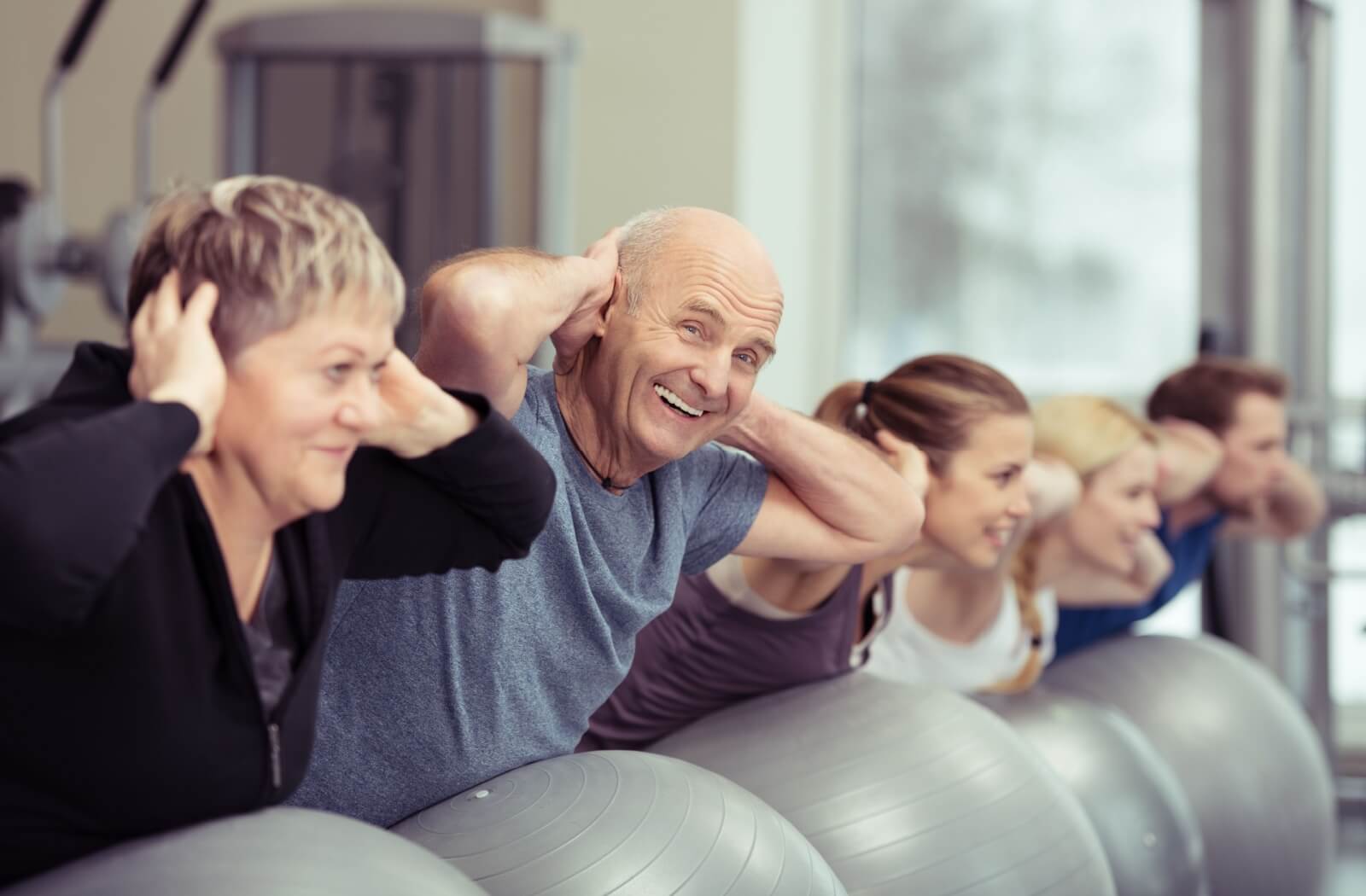 An older adult couple perform a balance exercise on a stability ball in a Pilates class.