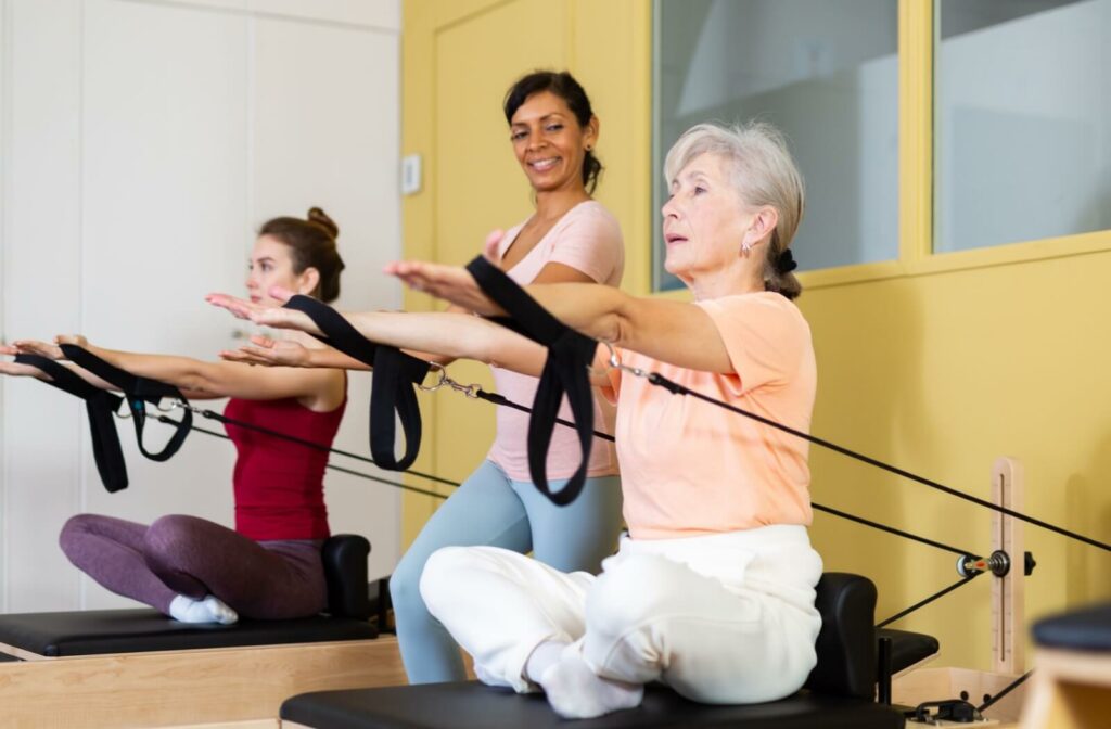 A community member engages in a Pilates class, stretching with bands under the attentive guidance of a caring instructor.