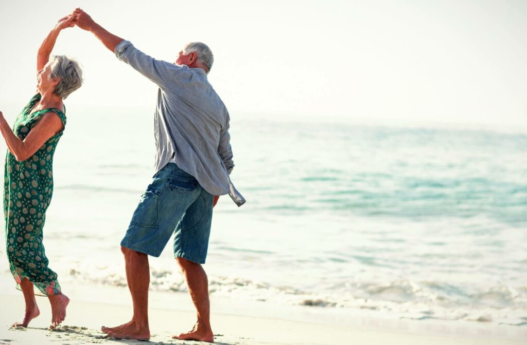 An older adult couple dance together on the beach.