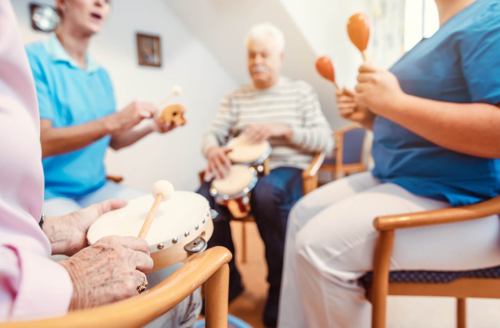 A group of older adults sitting in a circle participate in music therapy, each with their own instrument.
