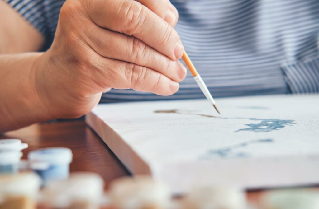 An older adult's hand grasping a paint brush, poised above a paint-by-numbers.