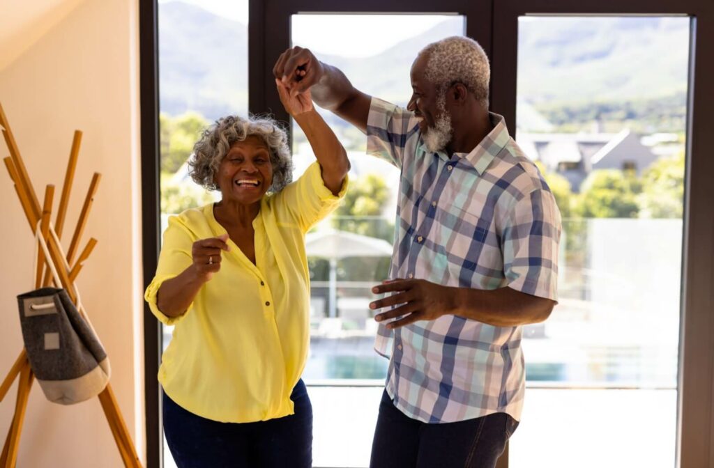 A joyful mature couple dance in the doorway of their independent living home.