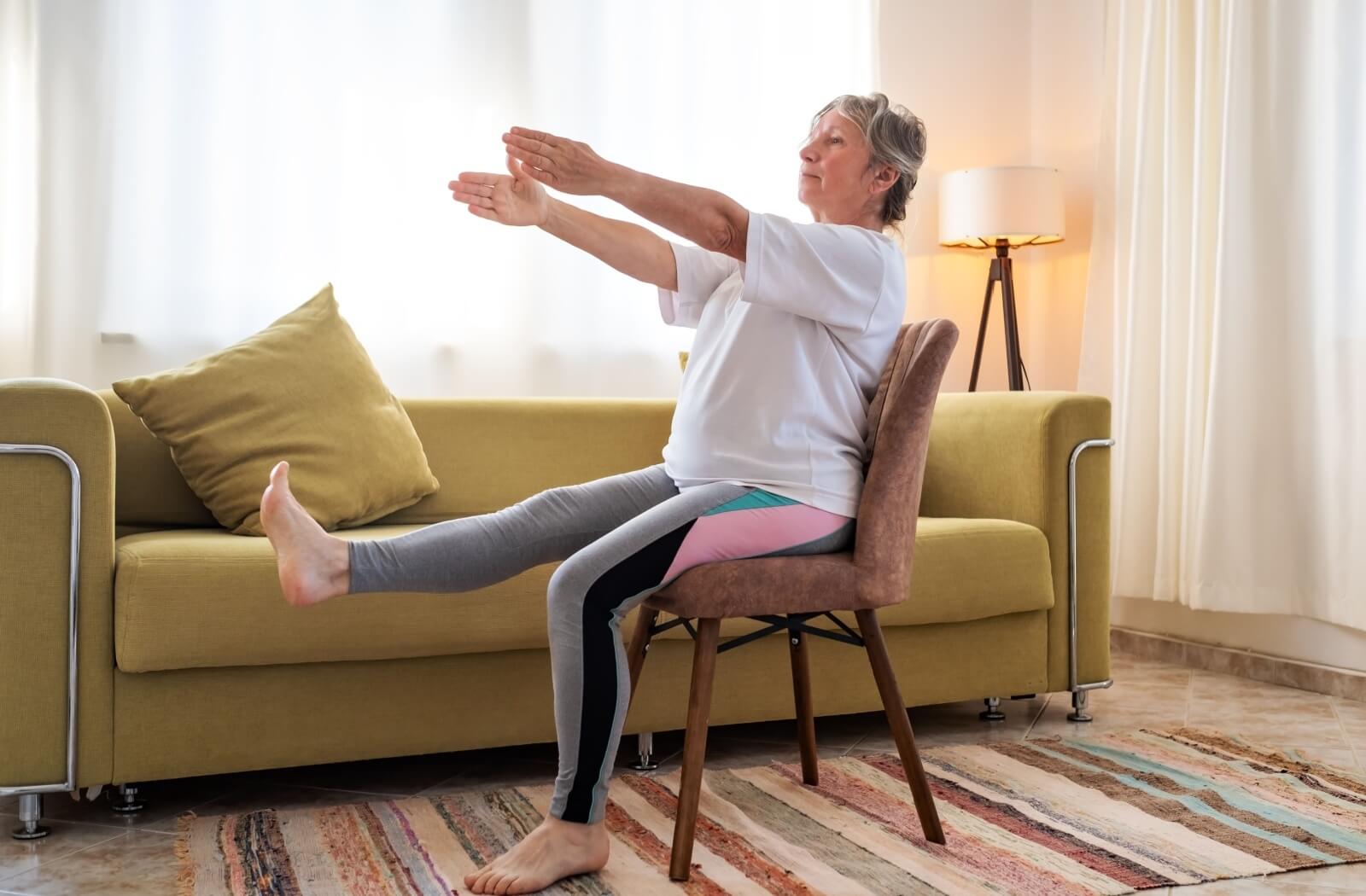 An older adult lifts their arms and one leg while participating in sitting tai chi.