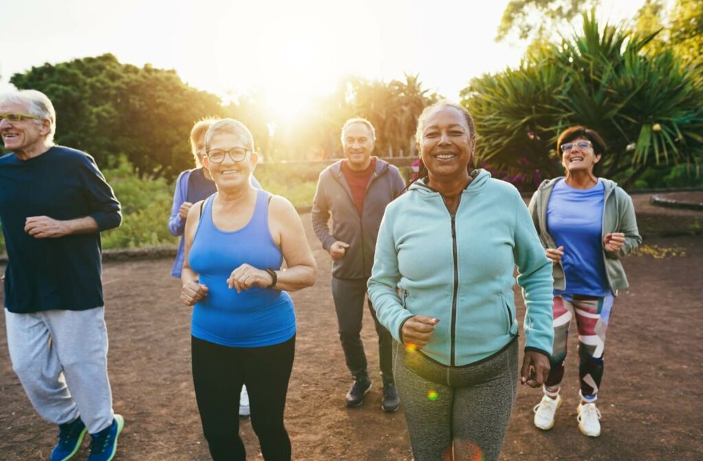 A diverse group of older adults jogging together outdoors at sunrise, smiling and enjoying an active lifestyle in nature.