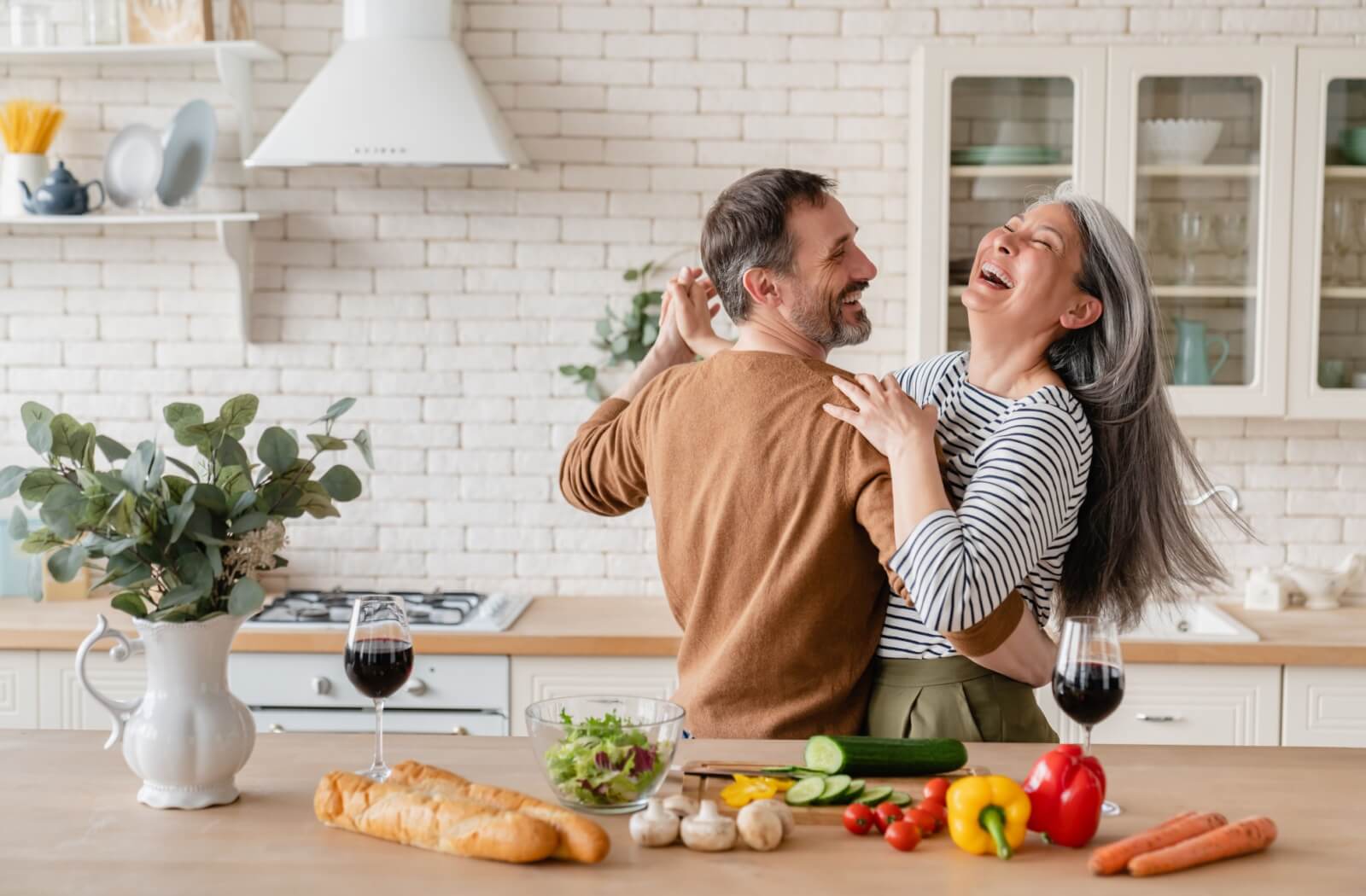 A joyful mature couple dance and laugh together in the kitchen.