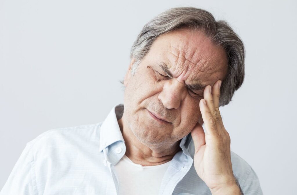 An older adult touching their temple with a pained expression, experiencing a headache.