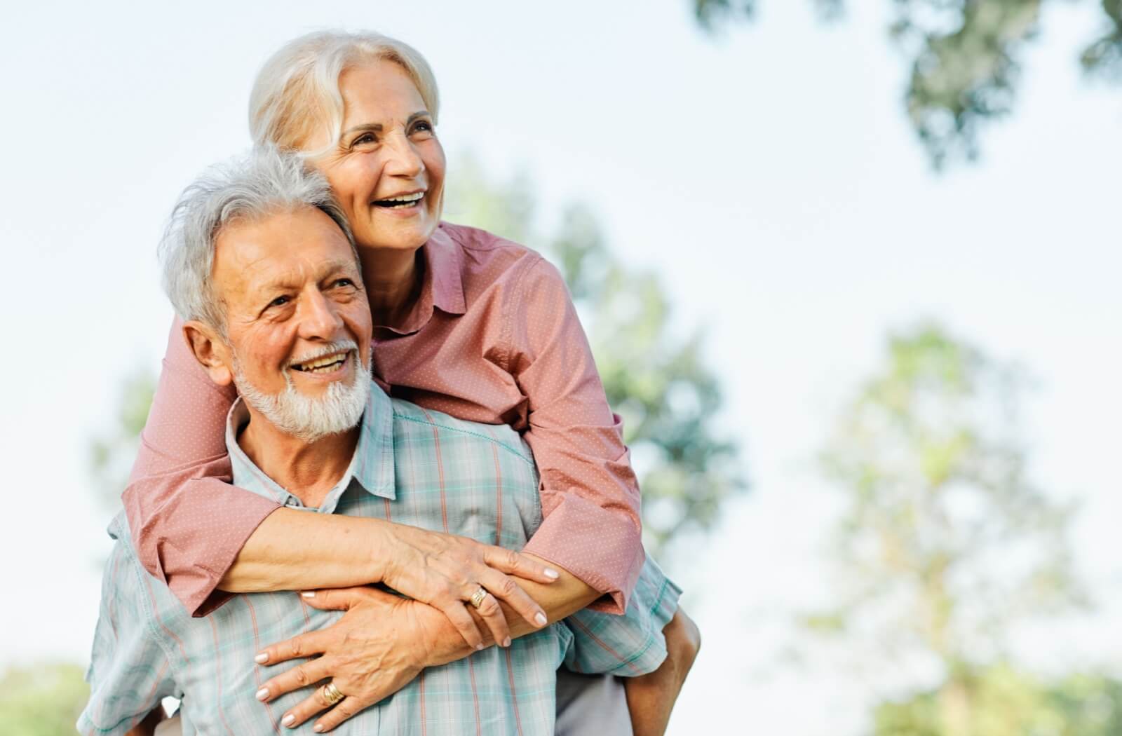 An older couple shares a joyful embrace outdoors, radiating love, happiness, and the warmth of growing older together.