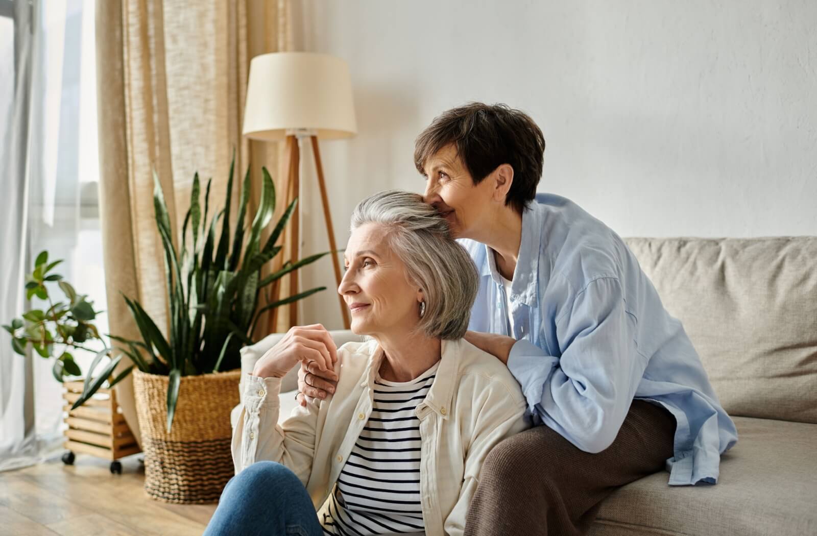 A mature couple hold hands while sitting in the living room.