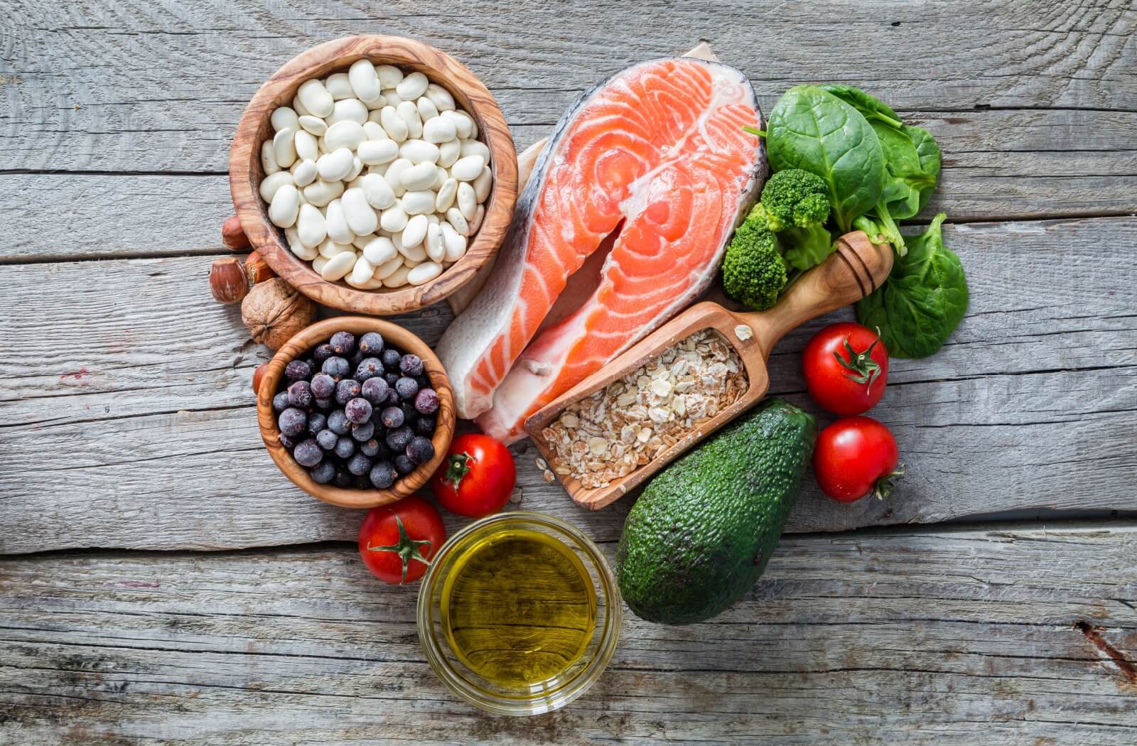 Several heart-healthy foods including fish, berries, and avocado are arranged artfully into a heart shape on a wooden background.