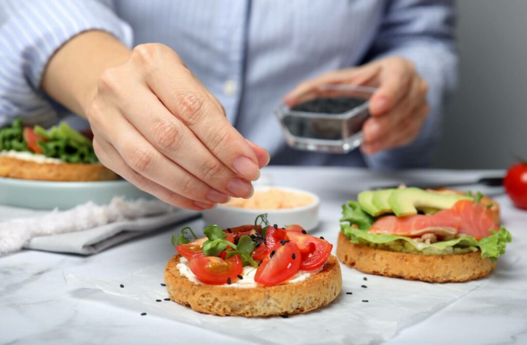 A person prepares a heart-healthy meal for lunch with salmon, avocado, leafy greens, and whole what bread.