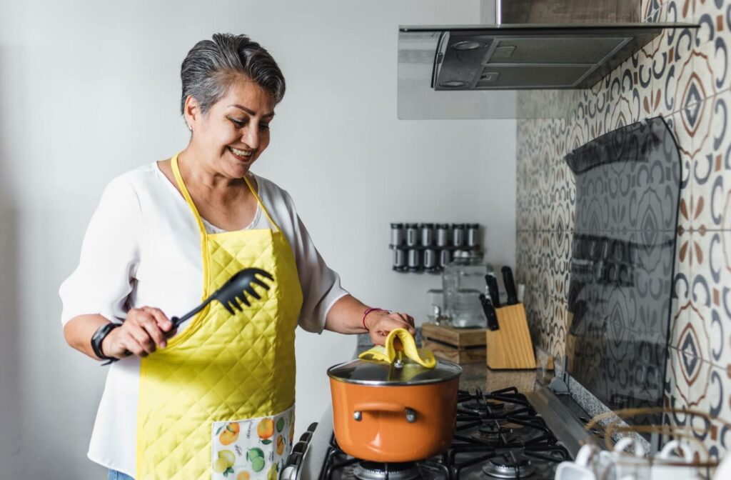 Senior woman cooking a protein-rich meal on the stove while wearing a yellow apron.