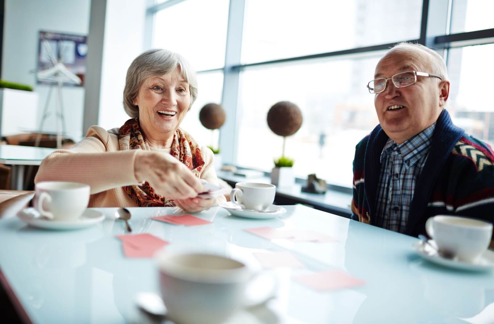 Two older adults enjoying a sit-down game together, sharing laughter over coffee.