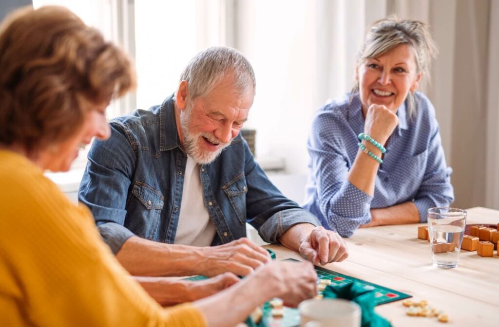 Three older adults enjoying a lively board game together at a table, having a good time.
