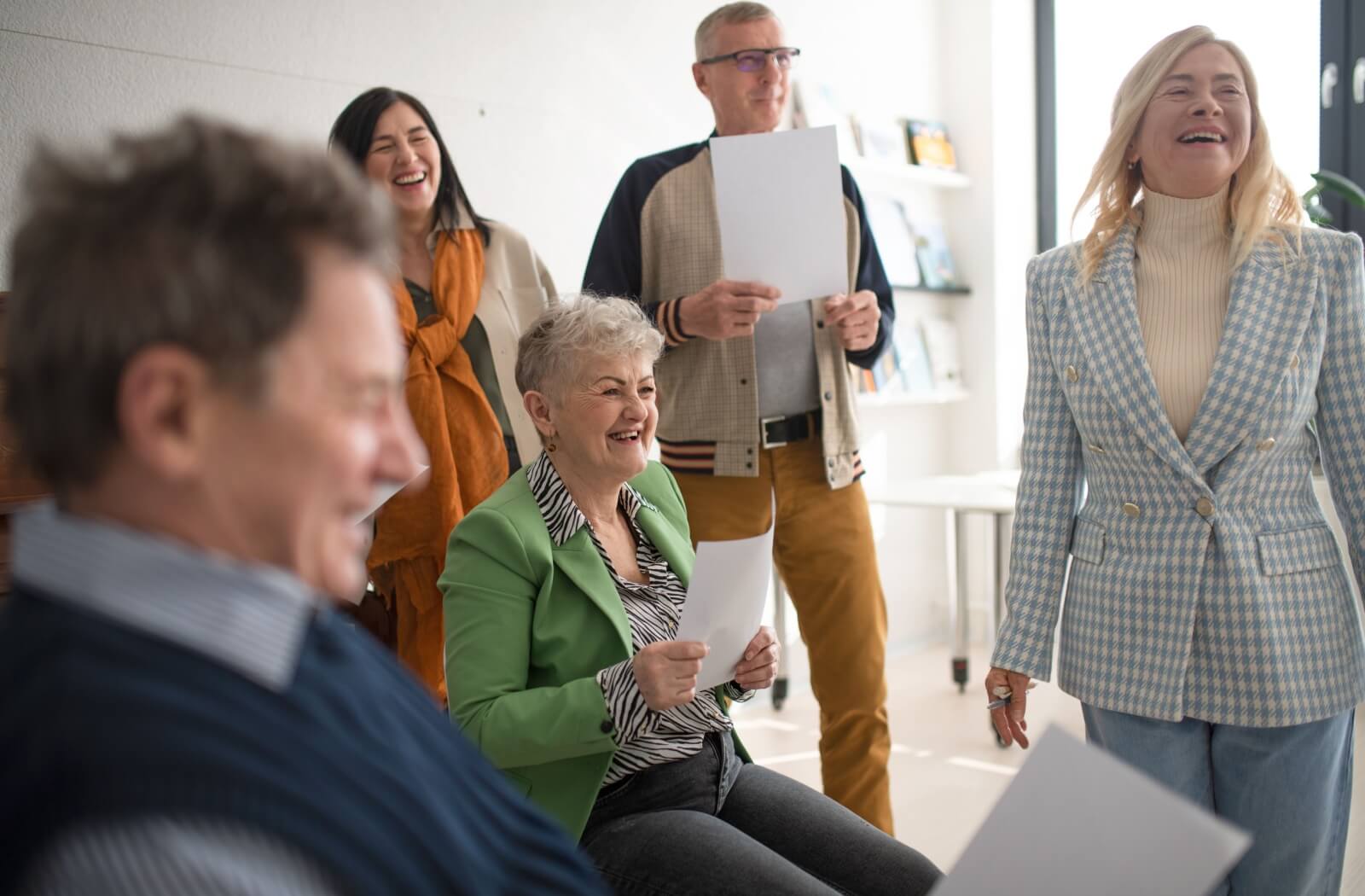 Group of older adults joyfully participating in a drama therapy session, holding scripts and engaging in storytelling.
