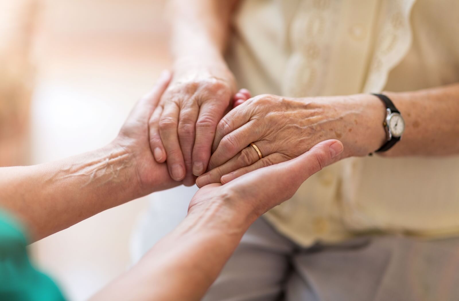 An adult child reaches out and embraces their senior parent's hands with their own after hearing about their parent's dementia diagnosis.