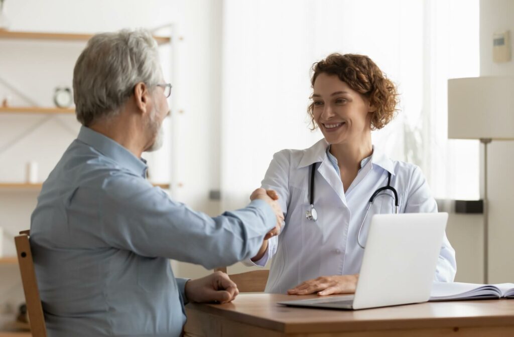 A doctor uses a laptop to access their older adult patient's electronic health records and send notes to their medical team.