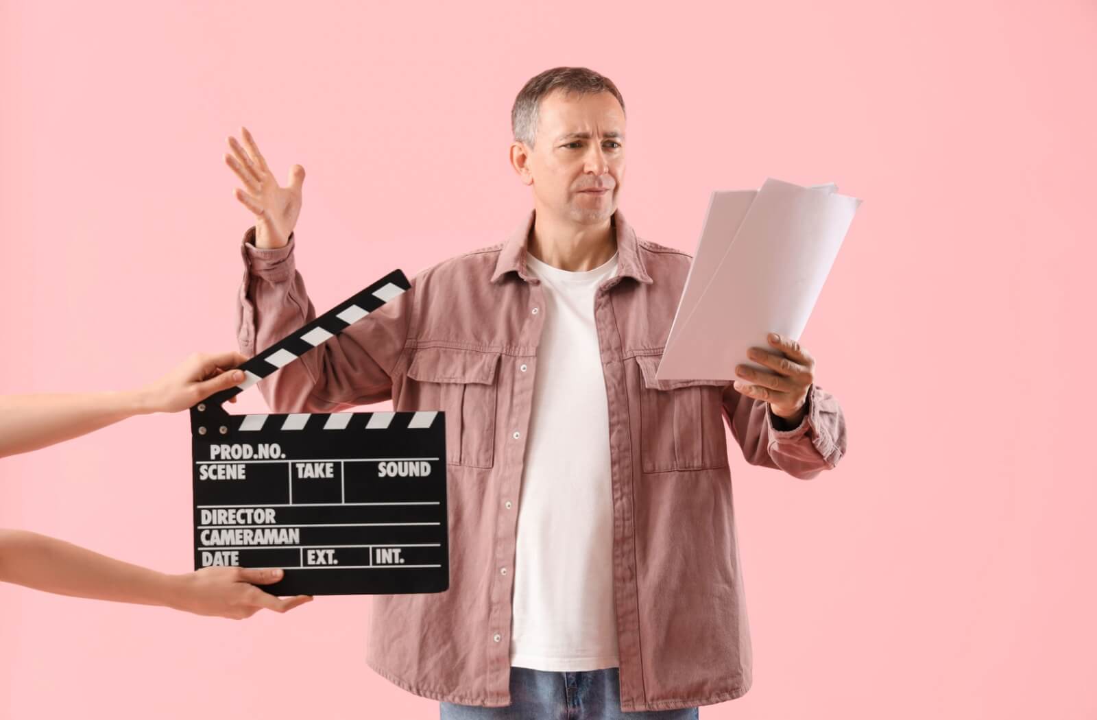 An older adult holds a script in front of them and raises their hand dramatically as they prepare to read lines for a play.