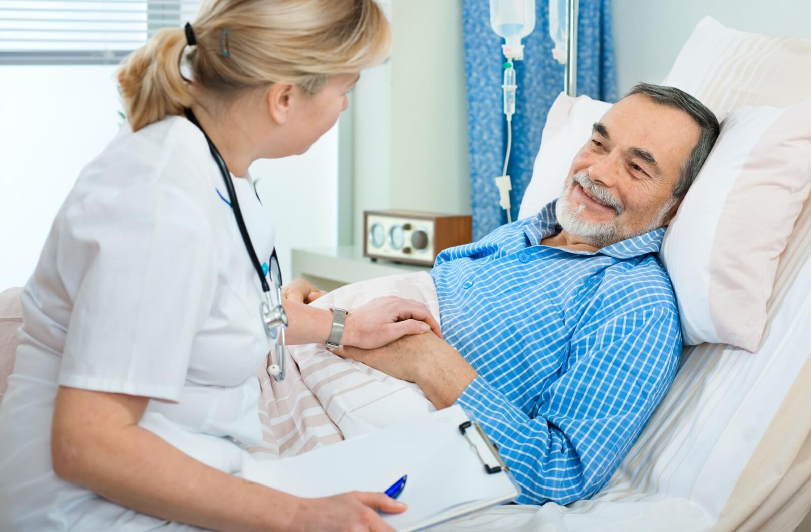 A nurse sits on the edge of their injured patient's bed to discuss the recovery process in a skilled nursing community.