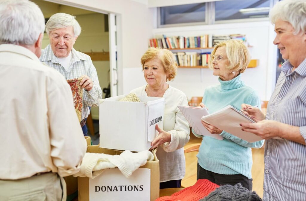 A group of senior volunteers sort through boxes of donations while chatting and smiling with each other.