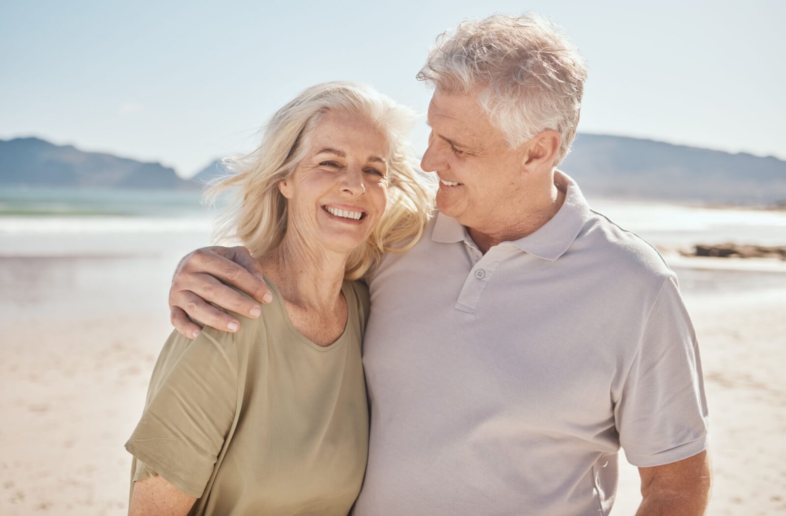 Two older adults enjoy a morning walk on the beach in the summer.