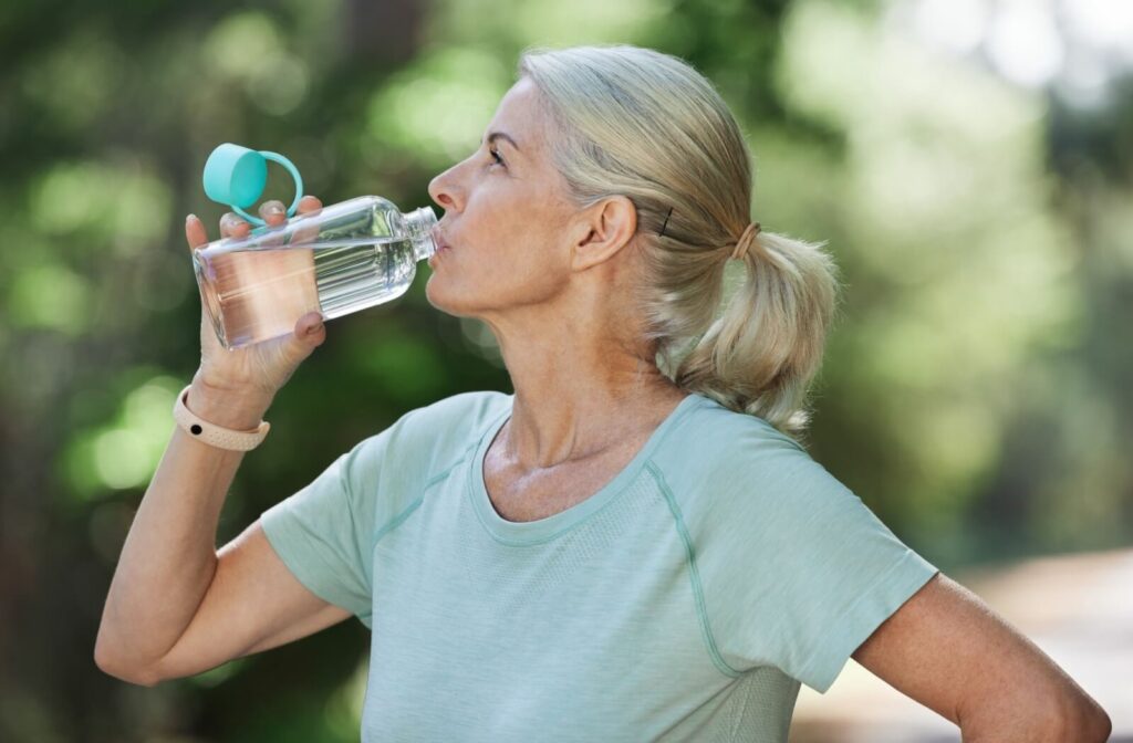An older adult sips from their water bottle to prevent dehydration in the summer.
