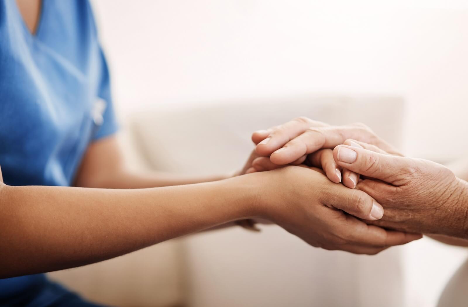 A caregiver clasping the hand of an older adult in memory care to reassure and support them.