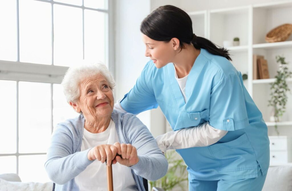 A caregiver checking on a resident in memory care, helping them to their feet and smiling.
