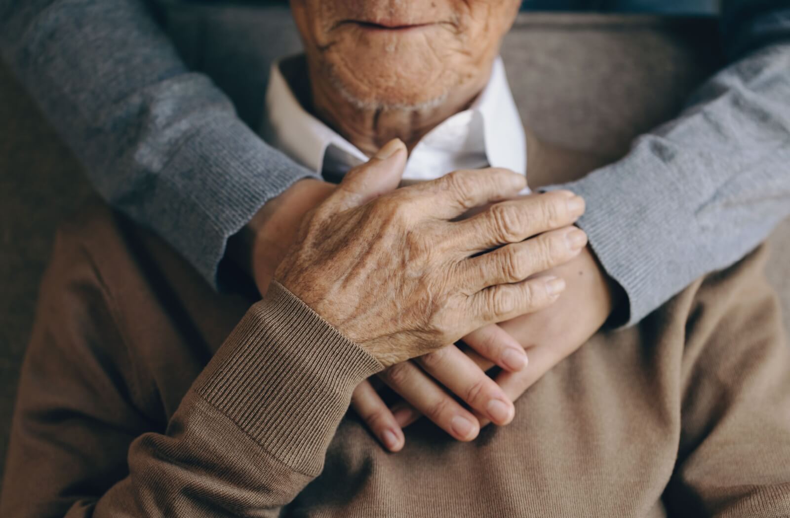 A close-up image of an adult child holding their older parent from behind to support and reassure them.
