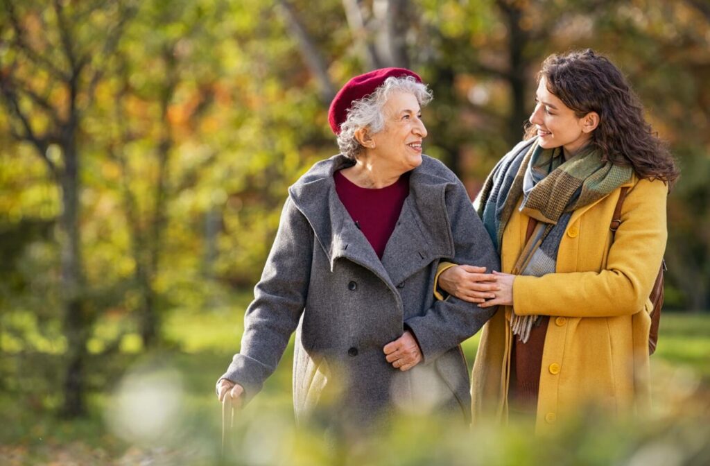An older adult and their adult child walking arm-in-arm through a park to support one another.