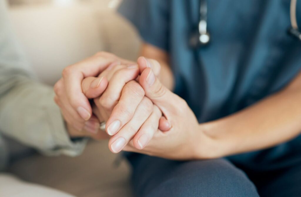 A caregiver in personal care clasping the hand of a community member to show support.