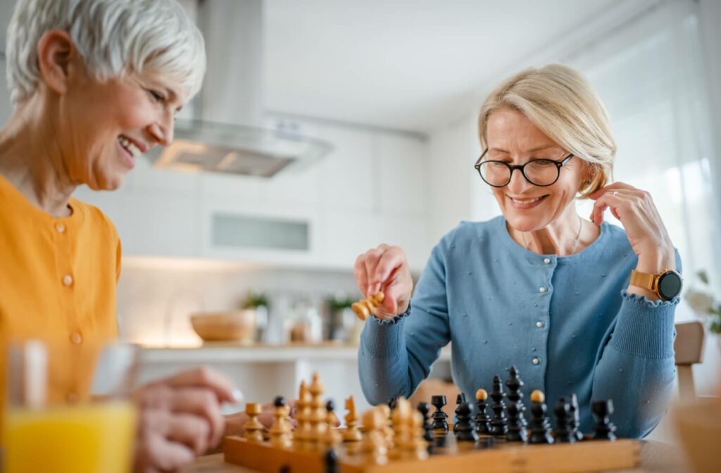 Two older friends playing chess in the kitchen of a home in independent living.