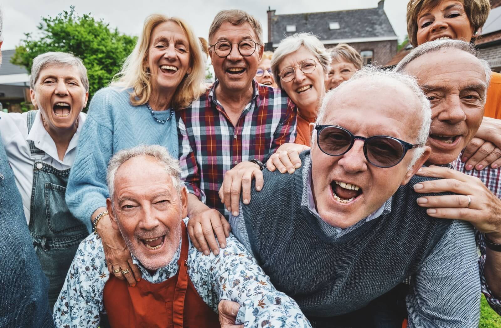 Group of older adults laughing and smiling outdoors leaning close together in a joyful group moment