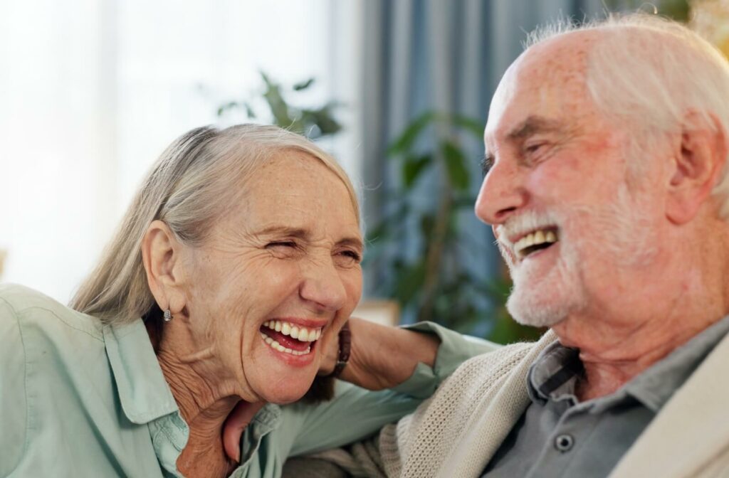 Two older adults laughing together indoors with warm expressions and relaxed body language