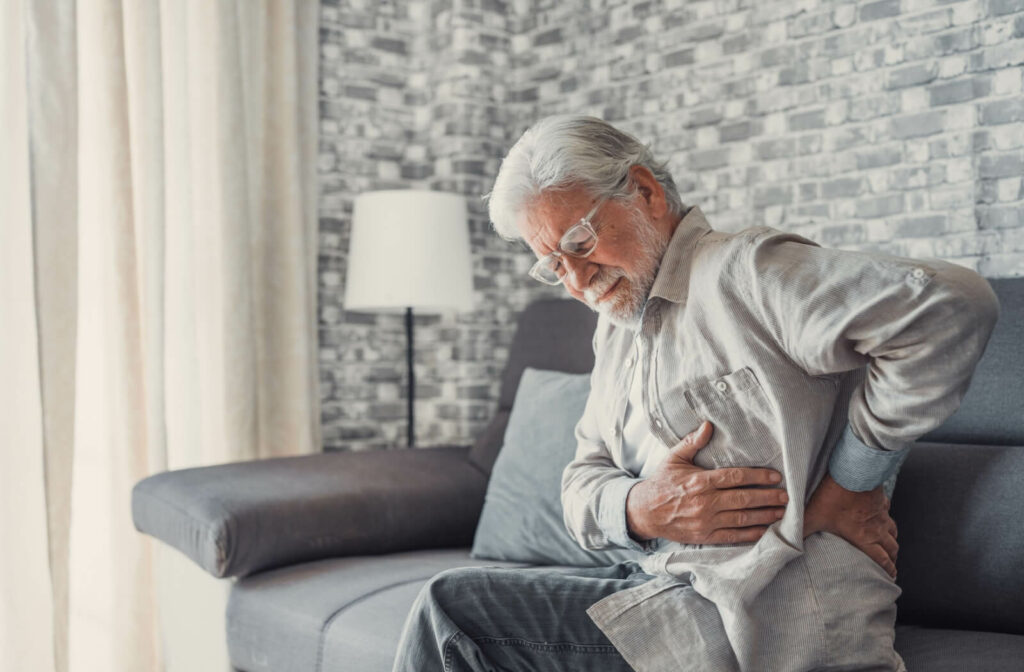 An older adult twisting to rub their hip due to chronic pain while sitting in their living room.
