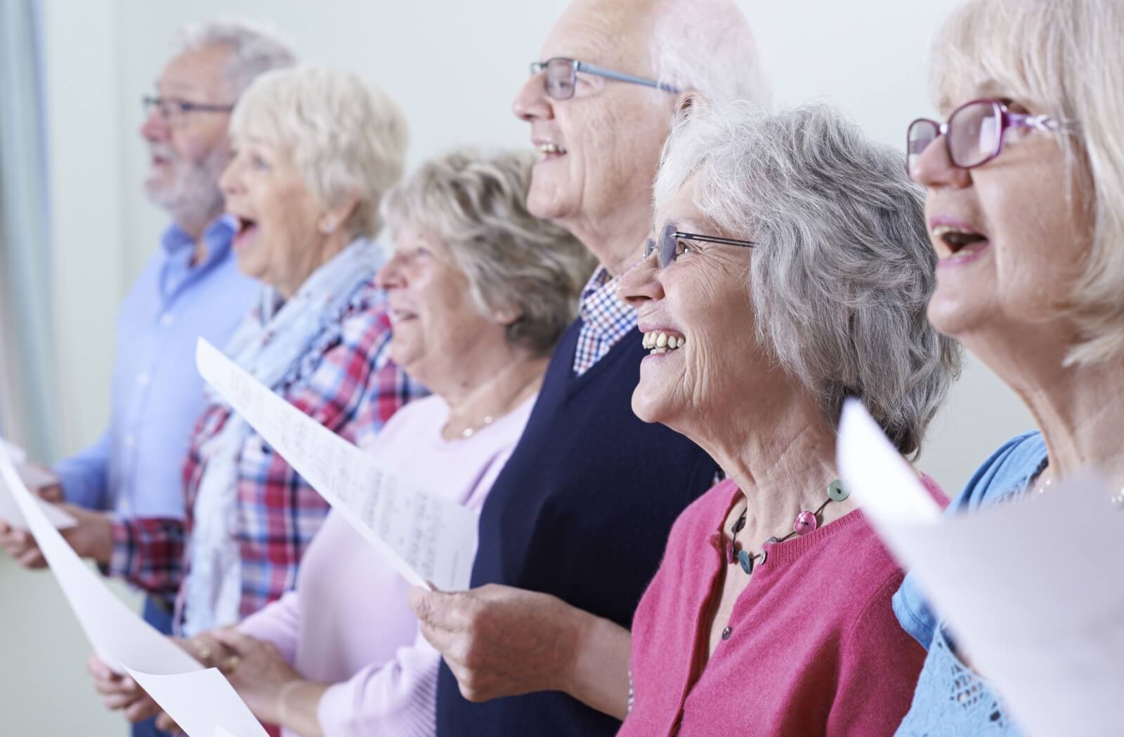 A lineup of older adults in senior living holding a song sheet and singing together while smiling.
