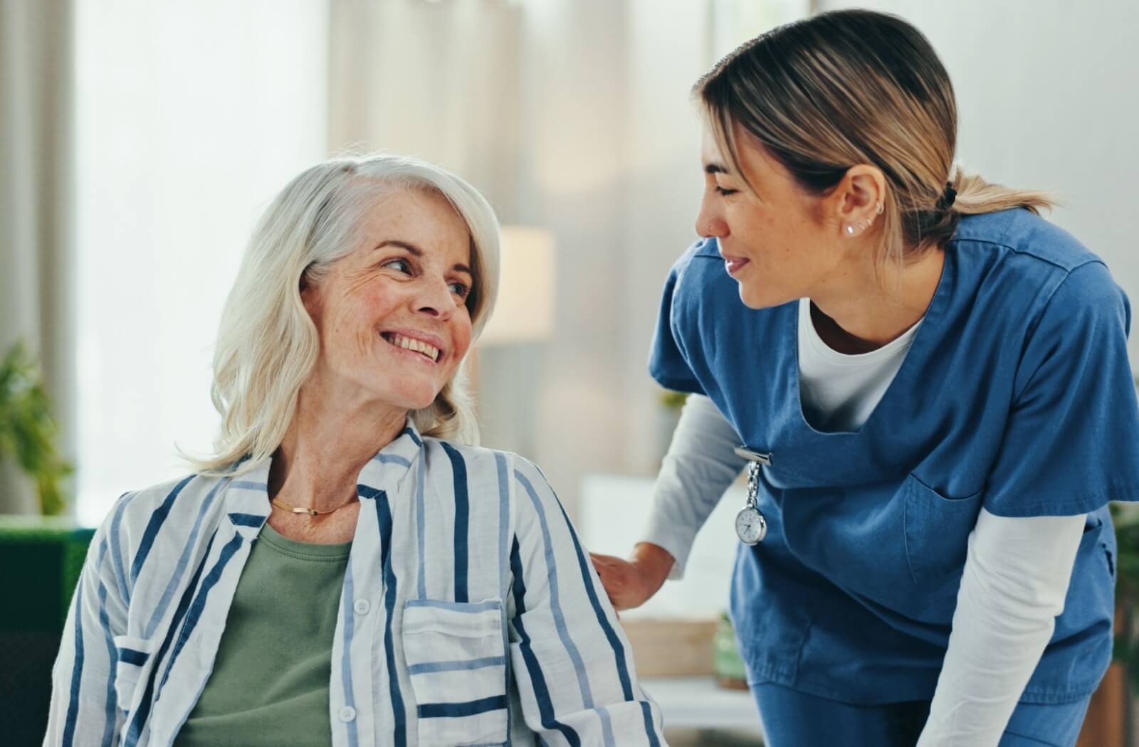 Older adult smiling at caregiver in scrubs during a warm friendly interaction in a bright supportive environment