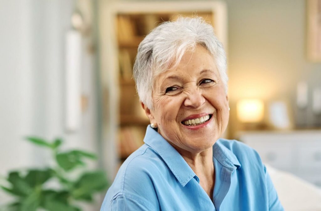 Older adult smiling warmly while sitting in a cozy indoor space with soft lighting and books in the background