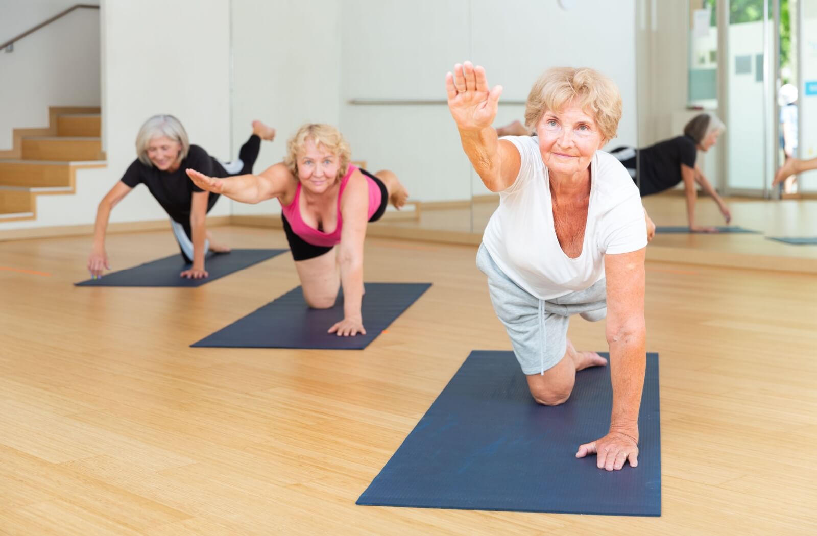 3 older adults stretching on yoga mats during an exercise class to help them with their balance.